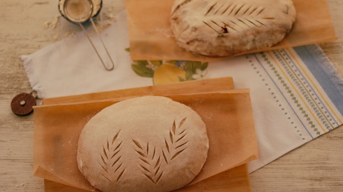 Freshly prepared artisanal bread dough with leaf score patterns on parchment paper.