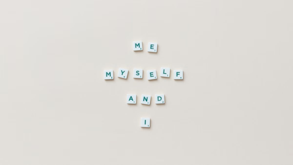 Minimalist composition of Scrabble tiles spelling 'Me, Myself, and I' on a white background.